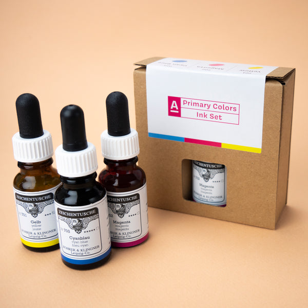 A photo of the Primary Colors ink set in its box and all three bottles included in the set next to it. The box has a small hole in the middle, through which the label of the color magenta can be seen.