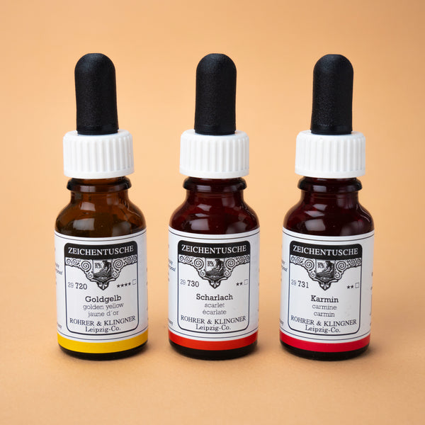 A photo of all three bottles included in this set next to each other: golden yellow, scarlet, and carmine. The bottles are made of dark brown glass with white labels and black rubber caps.
