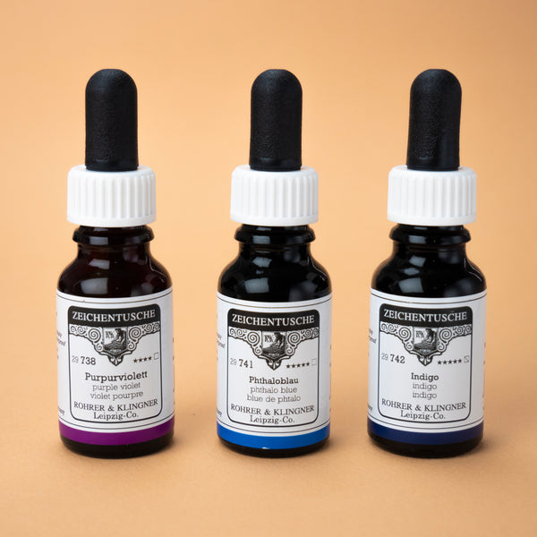 A photo of all three ink bottles included in this set next to one another: purple violet, phthalo blue, and indigo. The bottles are made from dark brown glass with white labels and a black rubber cap.