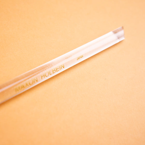 Photograph of a clear plastic burnishing tool, against a peach colored background.