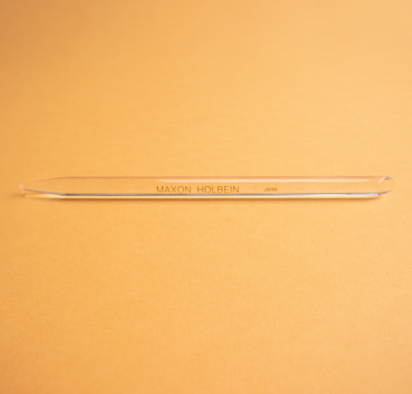 Photograph of a clear plastic burnishing tool, against a peach colored background.