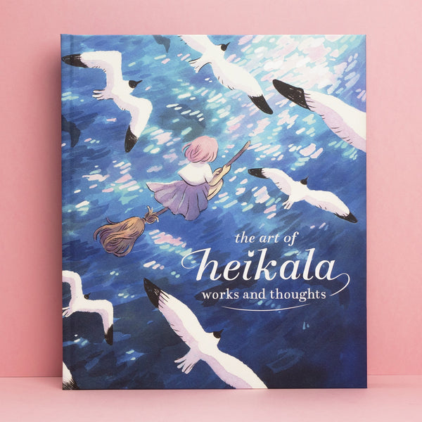 Photo of The Art of Heikala art book, a book with a blue cover, against a pink background.