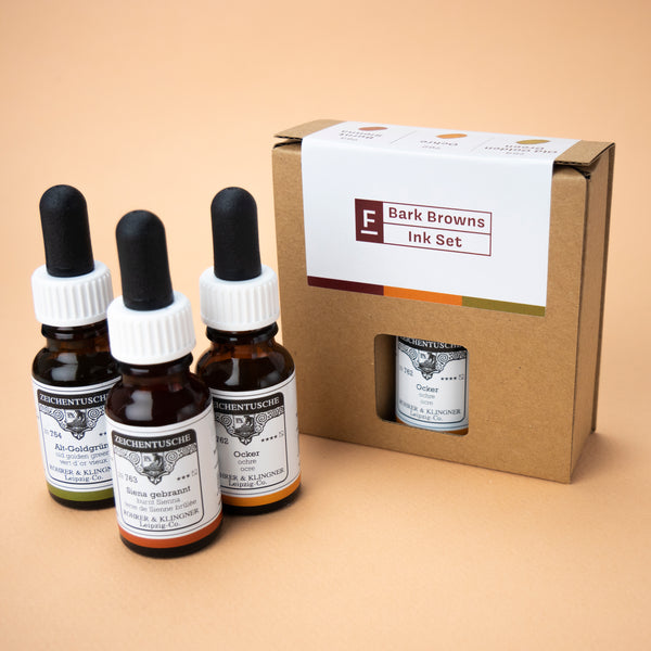 A photo of the Bark Browns ink set in its box and all three bottles included in the set next to it. The box has a small hole in the middle, through which the label of the color ochre can be seen.