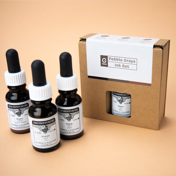 A photo of the Pebble Greys ink set in its box and all three bottles included in the set next to it. The box has a small hole in the middle, through which the label of the color sepia can be seen.