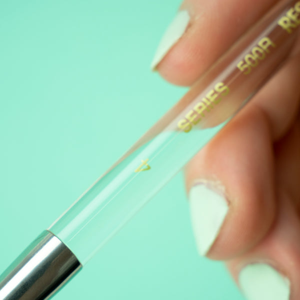 A closeup photo of the transparent handle of the size 4 brush, held in Heikala's hand against a turquoise background.