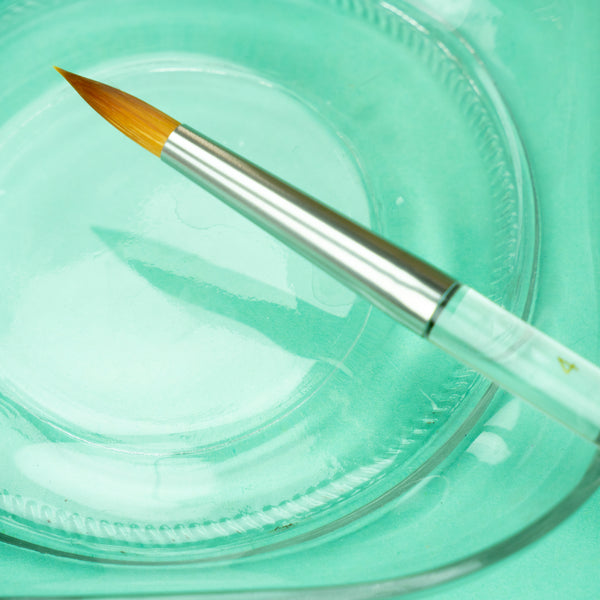 A closeup of the size 4 brush against a glass dish on a turquoise background.