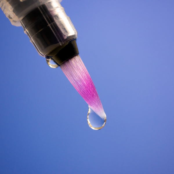 A closeup photo of the brush head of the Pentel Aquash Waterbrush, with drops of water against a blue background.