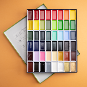 Photograph of a watercolor set with 48 different colors, against a peach colored background.