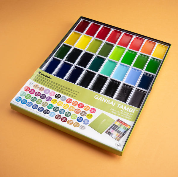 Photograph of a watercolor set with 48 different colors, against a peach colored background.