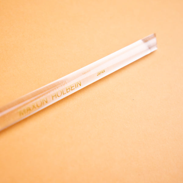 Photograph of a clear plastic burnishing tool, against a peach colored background. 